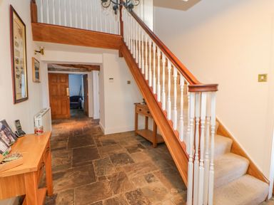 A hallway with a wooden staircase carpeted steps and tables along stone tile floor at East Farm House Humshaugh near Hexham