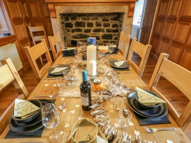 A wooden dining table set with plates utensils napkins candles and wine in a room with wood paneling and a stone fireplace at East Farm House Humshaugh near Hexham