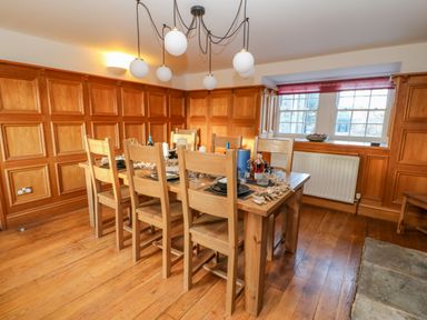 A dining room with a wooden table and chairs set up with plates and bottles near a window at East Farm House Humshaugh near Hexham