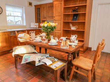 A kitchen with a wooden table set for breakfast with flowers newspapers and wooden chairs at East Farm House Humshaugh near Hexham