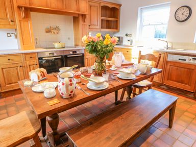 A kitchen with wooden cabinets and a wooden table set for breakfast with flowers on the table at East Farm House Humshaugh near Hexham