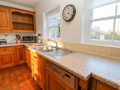 A kitchen with wooden cabinets a double sink a microwave and two windows at East Farm House in Humshaugh near Hexham