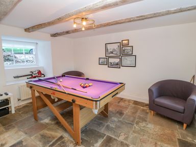 A game room with a purple pool table two chairs framed pictures on the wall a window and stone tile floor at East Farm House in Humshaugh near Hexham