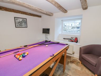 A games room with a purple pool table a chair a window and a screen on the wall at East Farm House in Humshaugh near Hexham