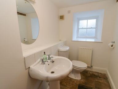 A bathroom with a sink, toilet, round mirror, window, and tiled floor at East Farm House in Humshaugh near Hexham