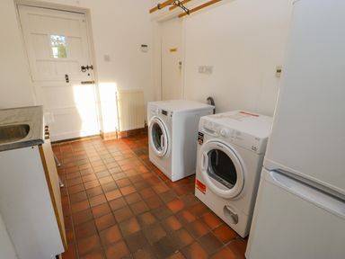 A utility room with a washing machine, dryer, refrigerator, sink, and white wooden door at East Farm House in Humshaugh near Hexham