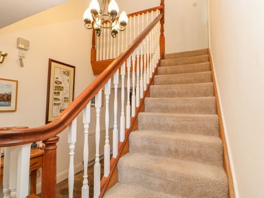 A carpeted staircase with wooden and white banisters and a chandelier at East Farm House in Humshaugh near Hexham