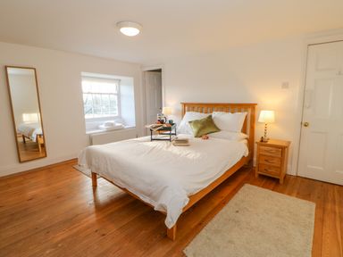 A bedroom with a wooden bed with white bedding and green pillow next to a window and a bedside table with a lamp at East Farm House in Humshaugh near Hexham