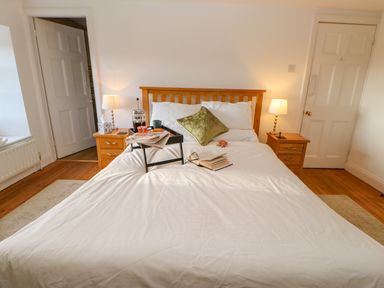 A bedroom with a wooden bed frame a white bedspread and bedside tables with lamps at East Farm House Humshaugh near Hexham