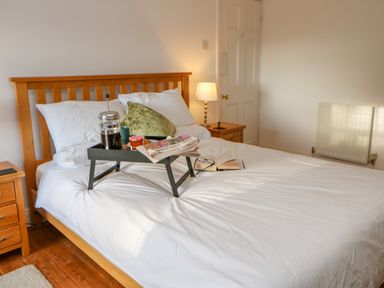 A bedroom with a wooden bed frame white bedding a tray with breakfast items on the bed and a lamp on a bedside table at East Farm House Humshaugh near Hexham