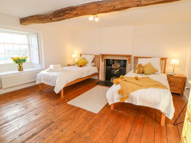 A bedroom with two single beds a fireplace wooden floor a window with flowers and bedside tables with lamps at East Farm House in Humshaugh near Hexham