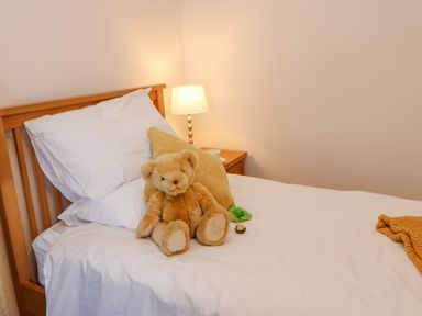 A bedroom with a wooden bed white bedding a teddy bear and a bedside table lamp at East Farm House in Humshaugh near Hexham