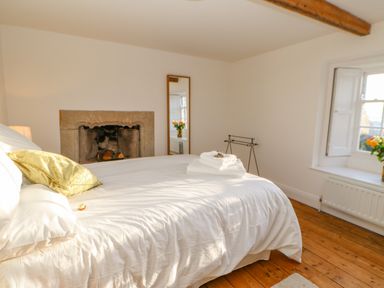 A bedroom with a white bed and folded towels near a fireplace and window at East Farm House in Humshaugh near Hexham