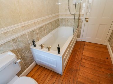 A bathroom with a bathtub, toilet, tiled walls, and wooden floor at East Farm House Humshaugh near Hexham