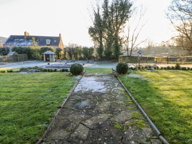 A garden with a stone pathway a small shed hedges and a house in the background at East Farm House in Humshaugh near Hexham