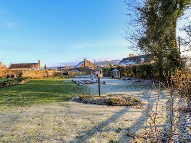 A garden with frost covered grass birdhouses stone buildings and hills in the background at East Farm House in Humshaugh near Hexham