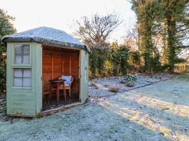 A small wooden garden shed with a chair and table inside on a frosty lawn surrounded by trees at East Farm House in Humshaugh near Hexham