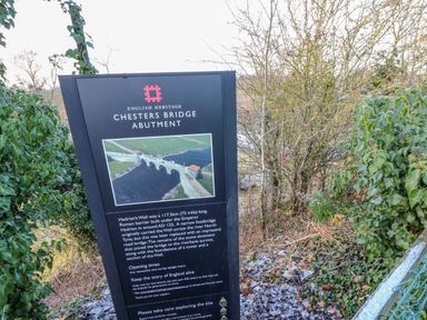 An information board about Chesters Bridge Abutment surrounded by trees and vegetation at East Farm House in Humshaugh near Hexham