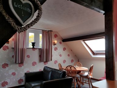 A sitting area with a black sofa a round wooden table with chairs floral wallpaper and a skylight window at The Coach House in North Newton near Bridgwater
