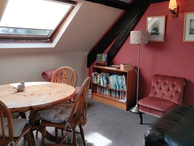 A room with a wooden dining table and chairs and a bookshelf against a red wall at The Coach House in North Newton near Bridgwater