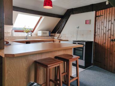 A kitchen with a wooden breakfast bar and stools a microwave and stove under a slanted window at The Coach House in North Newton near Bridgwater