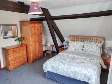 A bedroom with a wooden bed frame a floral bedspread wooden wardrobe chest of drawers and bedside tables with lamps at The Coach House in North Newton near Bridgwater