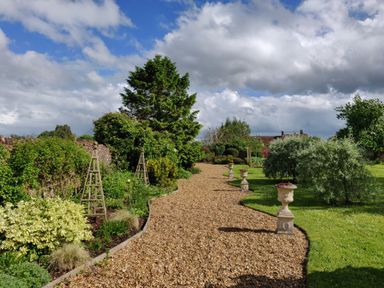 A garden with a gravel path bordered by plants and decorative urns at The Coach House in North Newton near Bridgwater