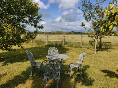 A metal table and four chairs on grass near trees and a wooden fence in a field at The Coach House in North Newton near Bridgwater