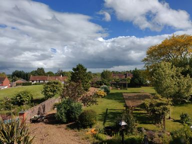 A garden with trees shrubs and a wooden pergola next to houses under a cloudy sky at The Coach House in North Newton near Bridgwater