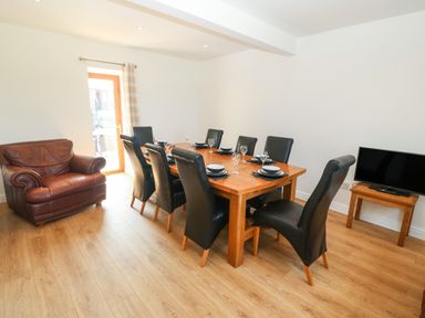 A dining room with a wooden table set for eight with black chairs a leather armchair and a television on a unit at Y Berth Ddu Farmhouse in Clynnog Fawr
