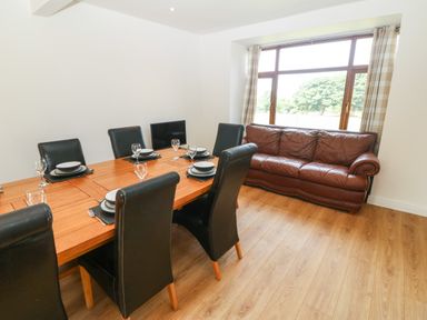 A dining area with a wooden table set for six and a brown leather sofa by a window at Y Berth Ddu Farmhouse in Clynnog Fawr