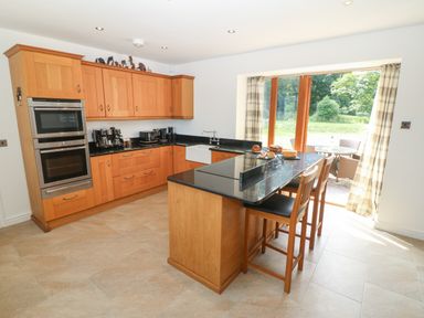 A kitchen with wooden cabinets black countertops an island with stools and a door leading to a garden at Y Berth Ddu Farmhouse in Clynnog Fawr