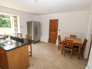 A kitchen with a wooden dining table and chairs a kitchen island with stools a refrigerator and a wooden door at Y Berth Ddu Farmhouse in Clynnog Fawr