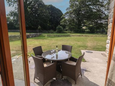 A patio with a round glass table and four wicker chairs overlooking a grassy yard at Y Berth Ddu Farmhouse in Clynnog Fawr