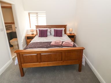 A bedroom with a wooden bed frame two bedside tables with lamps folded towels on the bed and an open door showing a toilet at Y Berth Ddu Farmhouse in Clynnog Fawr