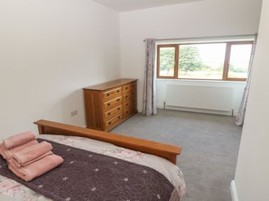 A bedroom with a wooden bed and dresser near a window with floral curtains at Y Berth Ddu Farmhouse in Clynnog Fawr