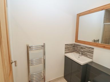 A bathroom with a sink, a large mirror, a towel radiator, and tiled walls at Y Berth Ddu Farmhouse in Clynnog Fawr