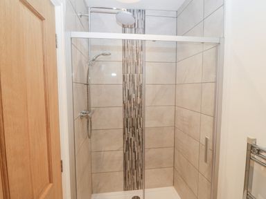 A tiled shower enclosure with a glass door and dual shower heads at Y Berth Ddu Farmhouse in Clynnog Fawr