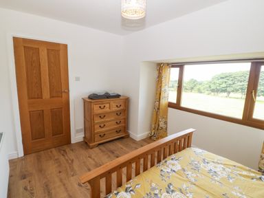 A bedroom with a wooden bed and dresser next to a window with floral curtains at Y Berth Ddu Farmhouse in Clynnog Fawr