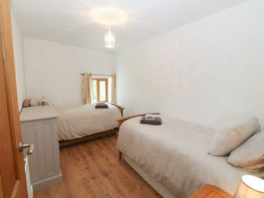 A bedroom with two single beds a small window and a wooden floor at Y Berth Ddu Farmhouse in Clynnog Fawr