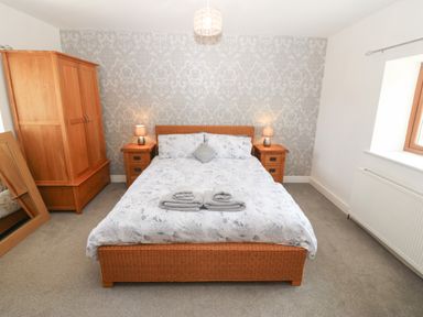 A bedroom with a double bed between two bedside tables with lamps and a wooden wardrobe with a mirror on the floor at Y Berth Ddu Farmhouse in Clynnog Fawr