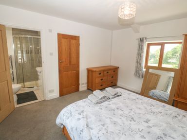 A bedroom with a bed a wooden dresser a mirror a window and an en suite shower room at Y Berth Ddu Farmhouse in Clynnog Fawr
