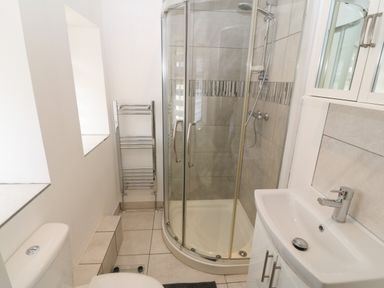A bathroom with a corner shower, a sink with cabinet, a toilet, and a towel rack at Y Berth Ddu Farmhouse in Clynnog Fawr