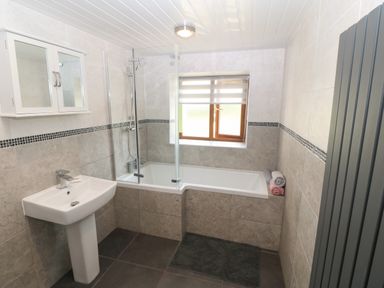 A bathroom with a bathtub shower combination sink wall cabinet window and towel rack at Y Berth Ddu Farmhouse in Clynnog Fawr