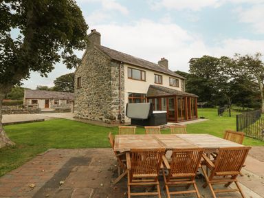 An outdoor patio with wooden table and chairs next to a stone farmhouse with green grass and trees at Y Berth Ddu Farmhouse in Clynnog Fawr