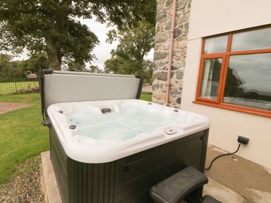 An outdoor hot tub with bubbling water next to a house with a stone wall and a window at Y Berth Ddu Farmhouse in Clynnog Fawr