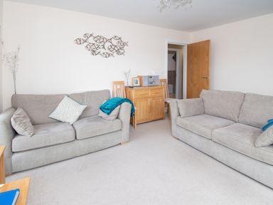 A living room with two sofas a wooden cabinet two chairs and an open door at The Moorings in Deganwy near Llandudno