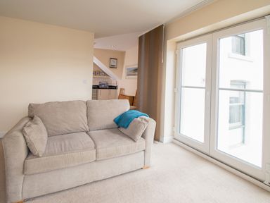 A living room with a beige sofa and blue throw next to glass doors at The Moorings in Deganwy near Llandudno