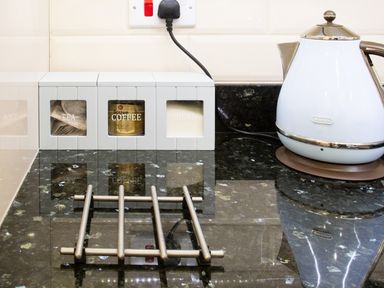 A kitchen countertop with canisters labeled tea coffee and sugar a kettle and a metal trivet at The Moorings in Deganwy near Llandudno