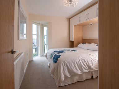 A bedroom with a double bed under built-in cupboards and a window at The Moorings in Deganwy near Llandudno